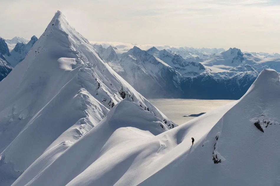 Des crêtes et sommets enneigés dominent une vallée au soleil couchant.