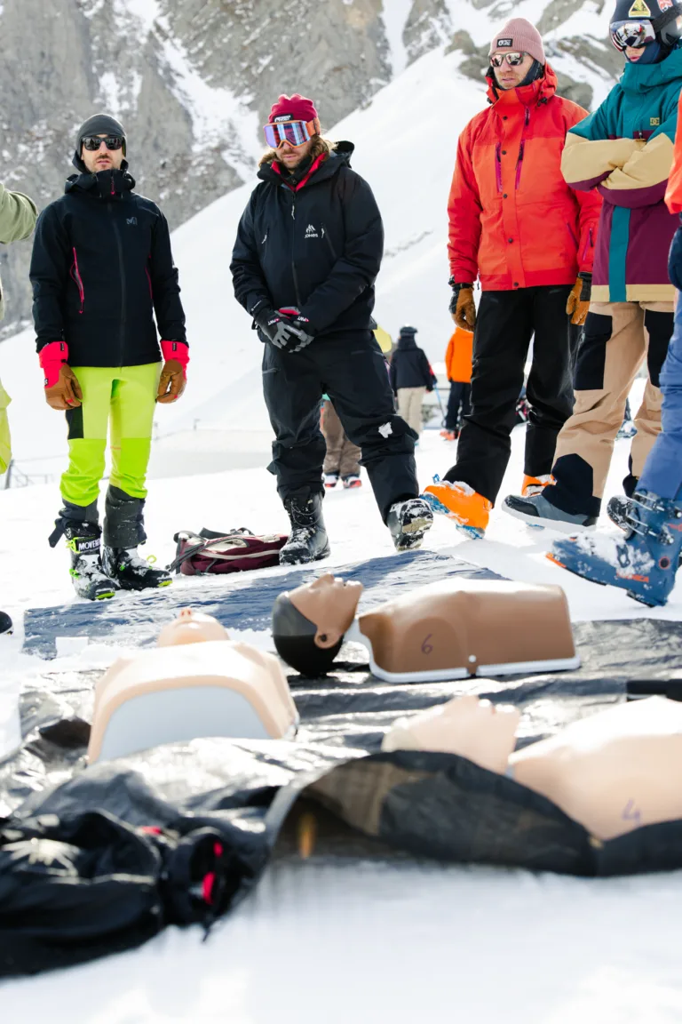 Des participants suivent un atelier de premiers secours autour d’un mannequin dans la neige.