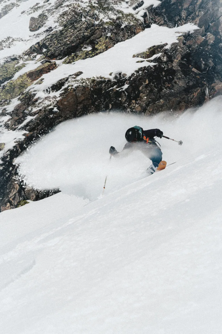 Un pratiquant de freeride descend dans la poudreuse à proximité de rochers.
