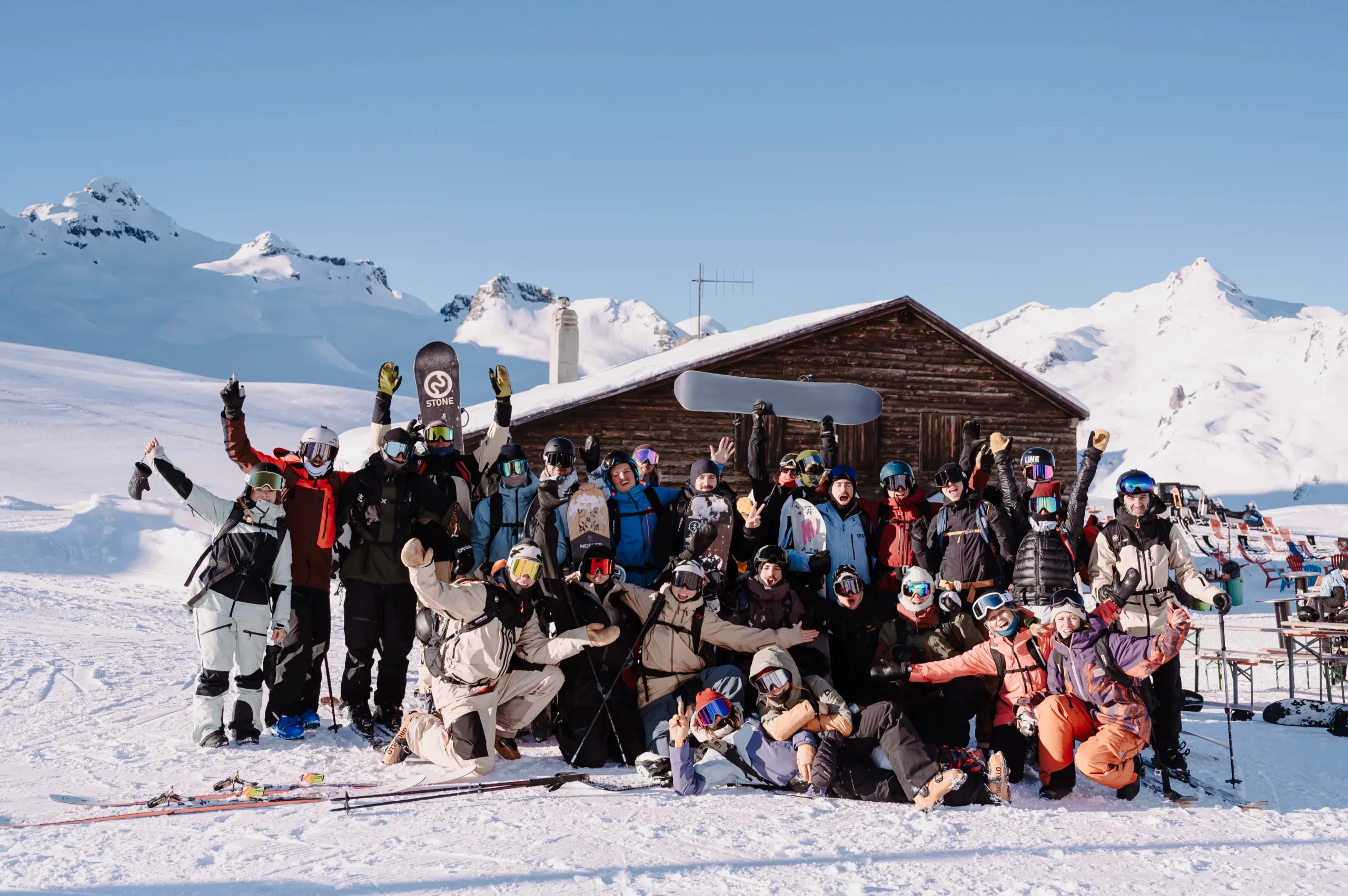 Groupe de skieurs et snowboardeurs réunis devant un chalet en montagne.