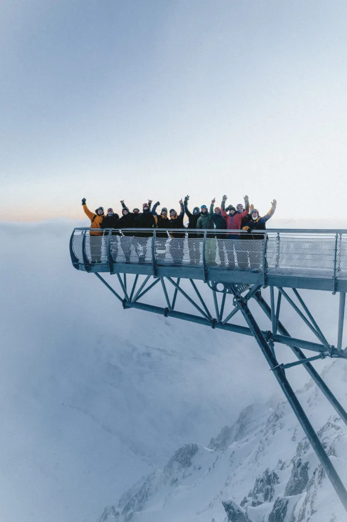 Un groupe lève les bras sur une passerelle panoramique au-dessus des montagnes.