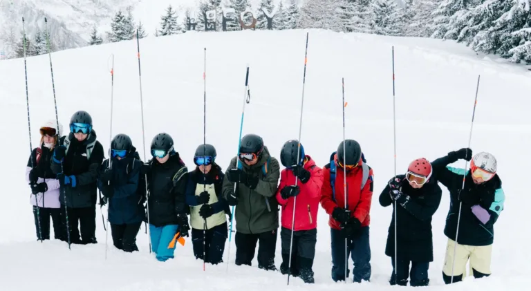 Des participants alignés dans la neige tiennent leurs sondes d’avalanche.