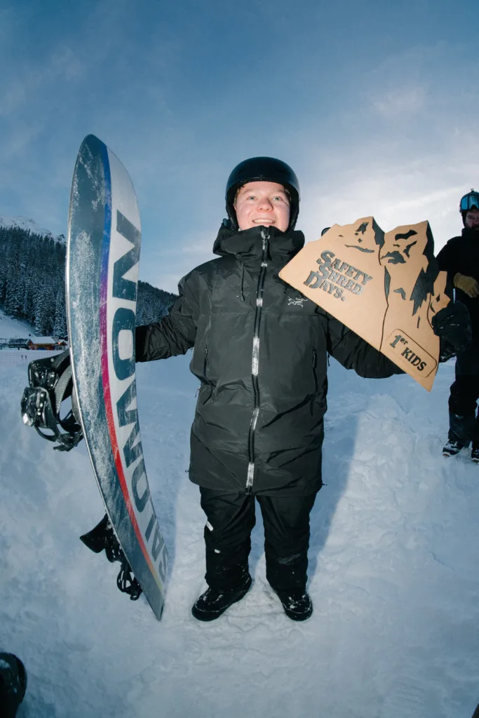 Un jeune participant pose dans la neige avec son snowboard et son matériel.