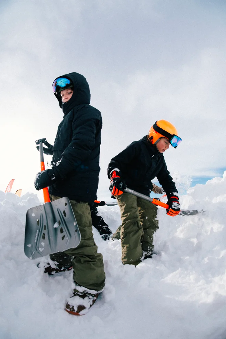 Deux participants équipés de pelles se tiennent dans la neige.