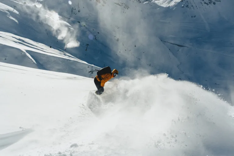 Un snowboardeur descend une pente de poudreuse en soulevant de la neige.