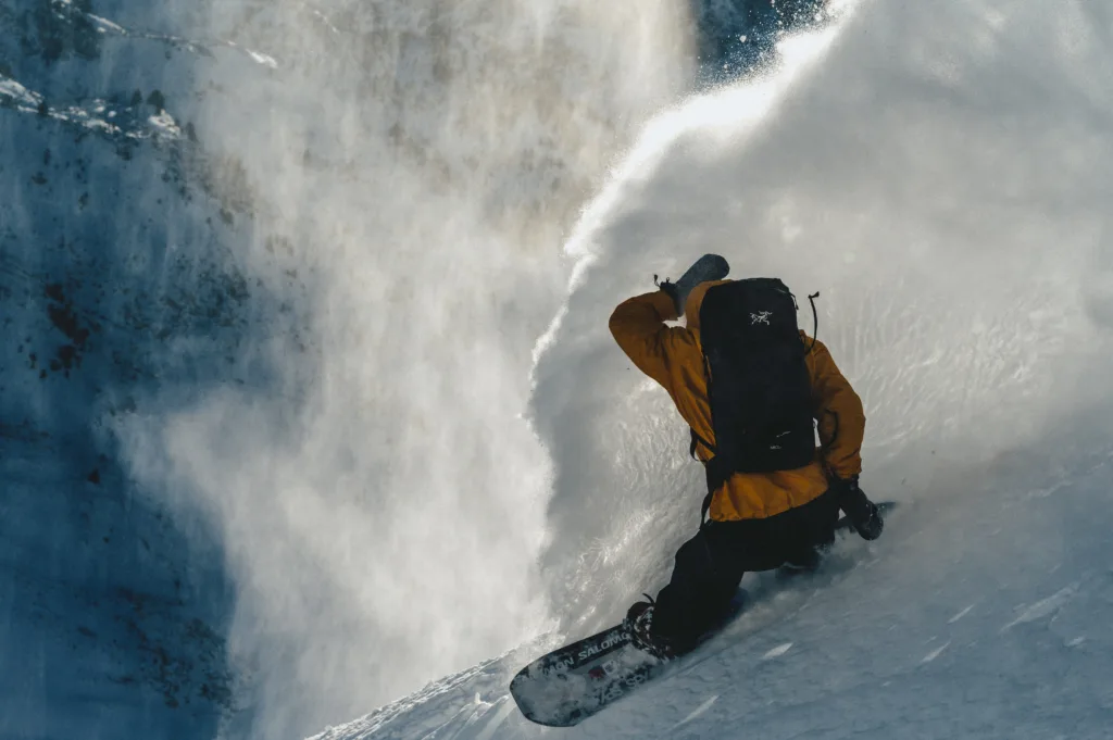 Un snowboardeur tourne dans la poudreuse au pied de parois rocheuses.