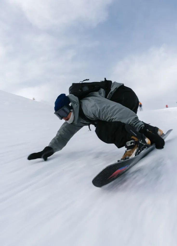 Un snowboardeur s’incline dans un virage et effleure la neige de la main.