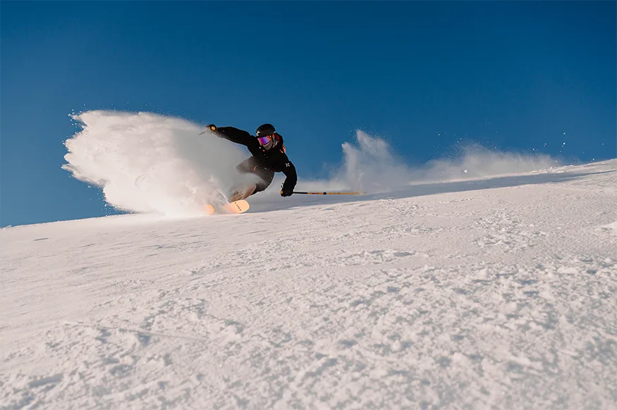 Un snowboardeur soulève un nuage de neige en tournant sur une pente ensoleillée.