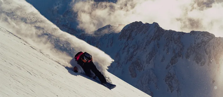 Un snowboardeur trace un virage dans la poudreuse sur une pente ensoleillée.