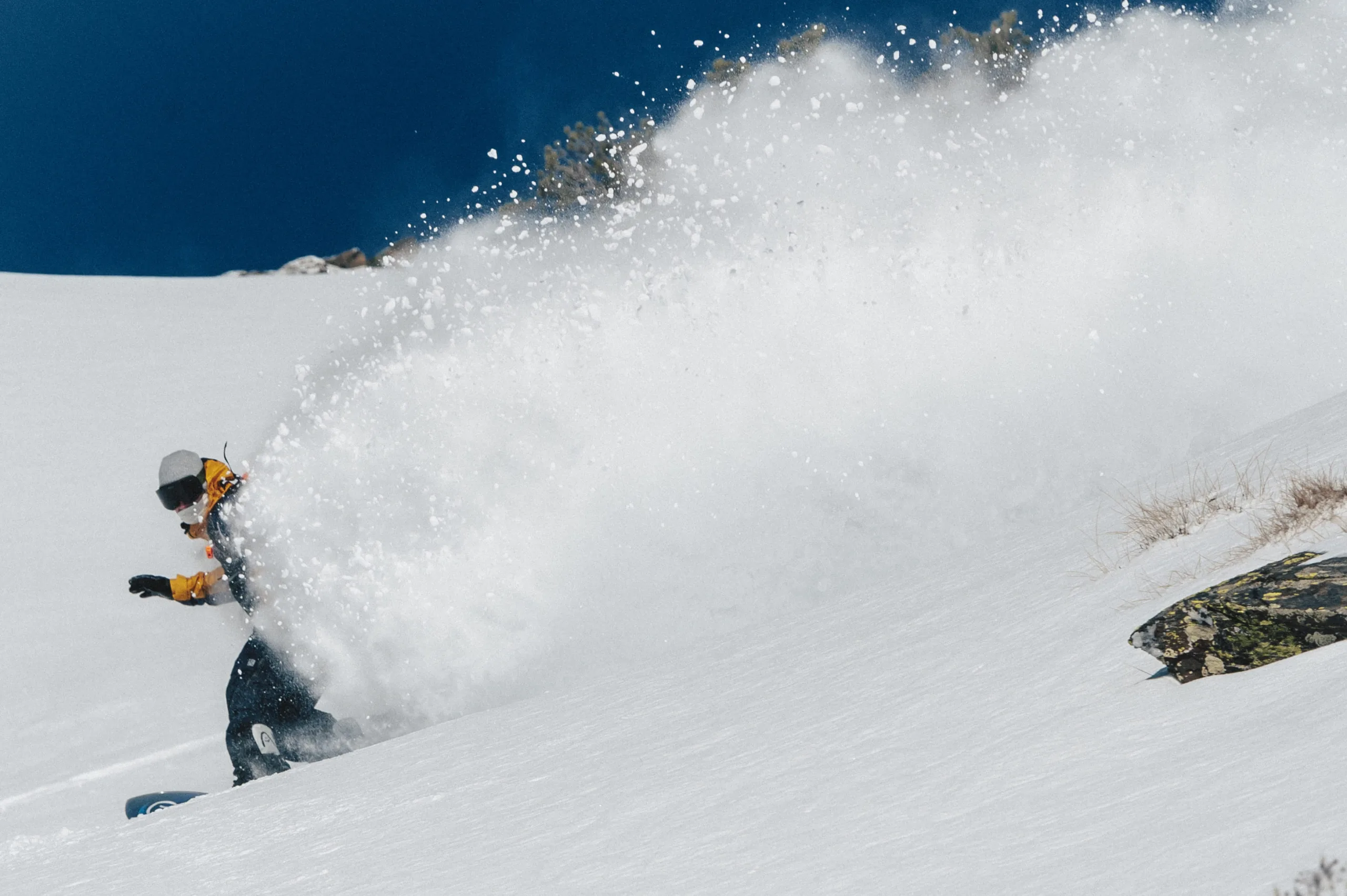 Un snowboardeur effectue un virage en soulevant un grand nuage de poudreuse.